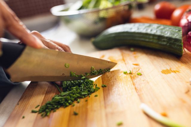 Cropped hands of biracial mature woman chopping fresh green vegetables on cutting board in kitchen. Unaltered, food, organic, cooking, preparation, home, lifestyle and retirement concept.