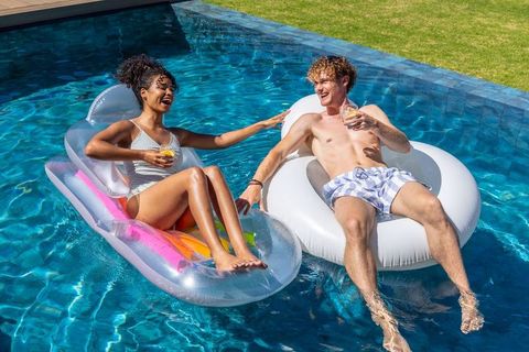 Laughing couple floating on colorful pool inflatables holding drinks for summer fun
