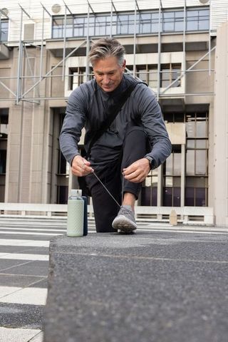 Middle-aged man tying shoelace on urban ledge preparing for run with reusable bottle