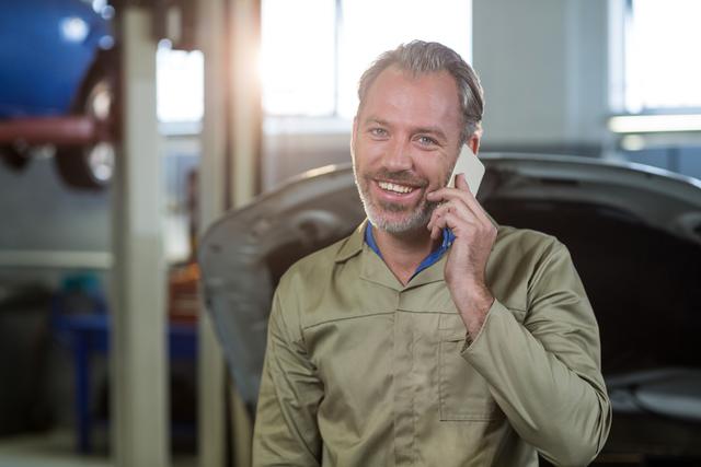 Smiling mechanic talking on a mobile phone - Download Free Stock Photos Pikwizard.com