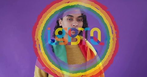 Nonbinary person posing wearing mustard sweater draping pride flag with rainbow overlay