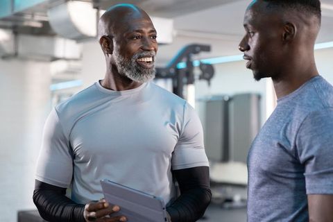 African american trainer coaching young athlete in modern gym holding tablet, smiling