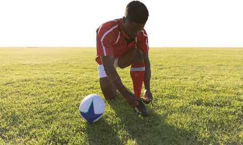 Young rugby player tying laces on green field, transparent background