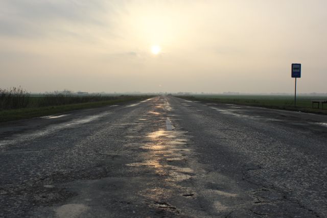 This visual portrays a tranquil and empty rural road during the early hours of dawn with a serene sunrise and distant fog. Ideal for use in themes of solitude, travel, and peaceful nature scenes, it can serve as background in presentations or as a calming conceptual metaphor for vast possibilities and unknown journeys.