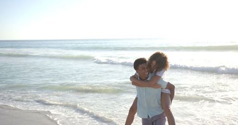 Playful Couple Enjoying Piggyback Ride on Sunny Beach Day