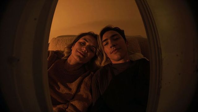 Warm intimate couple lounging on couch framed by rounded porthole, cozy evening mood