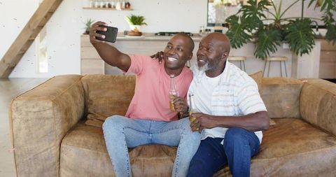 Father and Son Taking Selfie on Couch Sharing Drinks and Laughing in Bright Living Room