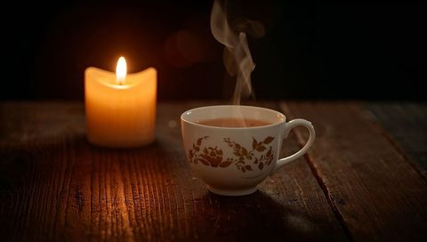 Steaming Floral Teacup on Rustic Wooden Table with Glowing Pillar Candle for Cozy Mood