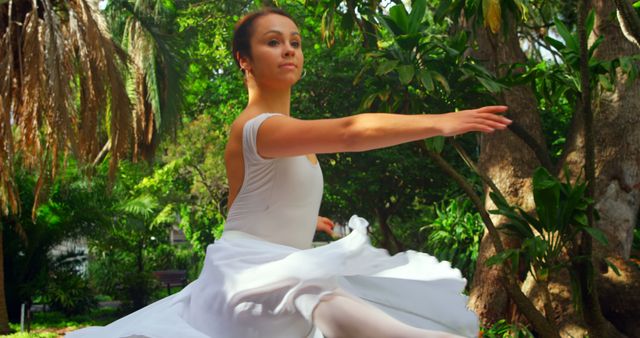 A young Caucasian ballerina performs a dance move in a lush garden, with copy space. Her graceful pose and the natural setting create a serene and artistic atmosphere.