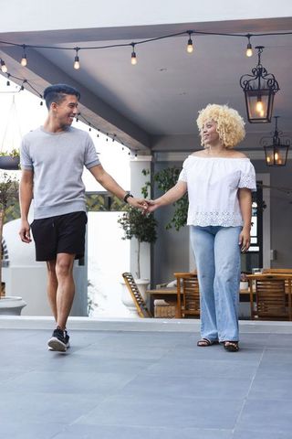 Couple walking hand-in-hand on covered patio with string lights and lanterns casual romance vibe