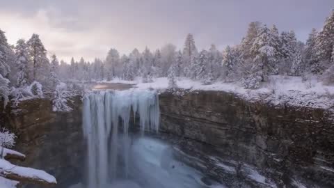 Panning drone revealing frozen waterfall plunging into snowy canyon with towering icicles