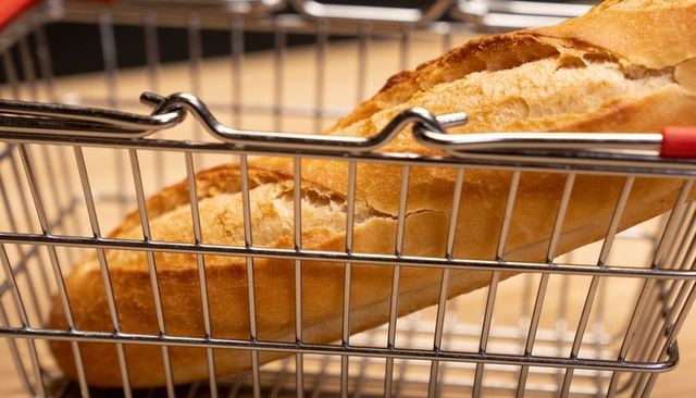 Crusty baguette resting in metal shopping basket on wooden counter for bakery display