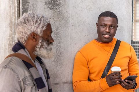 African american men having casual street conversation while holding coffee and smartphone