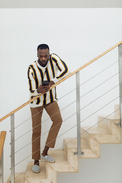 Front view of an African-American man using a smartphone while standing against the wooden rail of the stairs