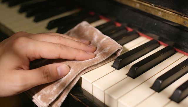 Polishing vintage piano keys using velvet cloth close-up, hand cleaning glossy keyboard