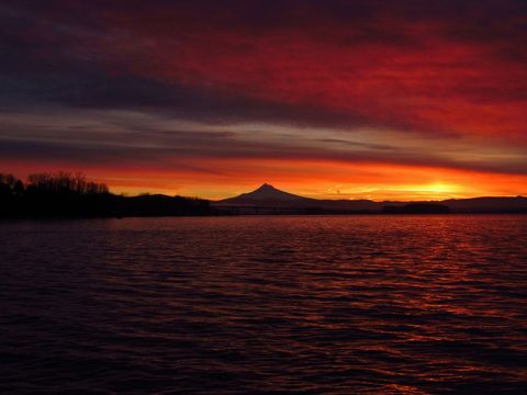 Crimson sunset glowing over mountain silhouette with bridge and water reflecting fiery sky