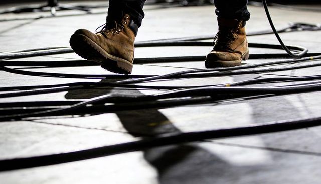 Stepping work boots amid tangled stage cables dramatic backstage rehearsal lighting and shadow