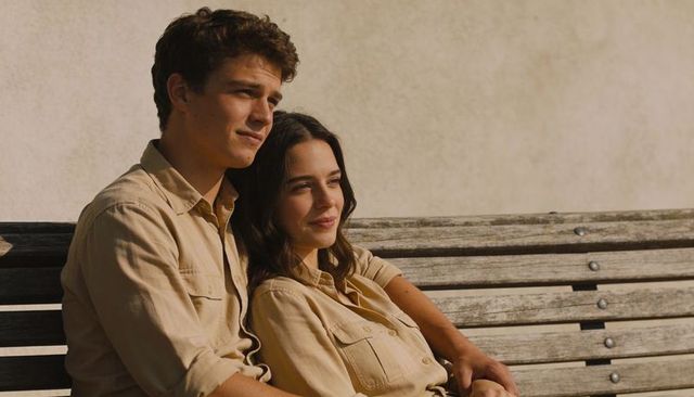 Young couple wearing matching beige shirts leaning and gazing on wooden bench in sunlight