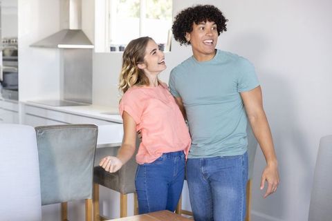 Young couple laughing and smiling in bright modern open-plan kitchen celebrating home