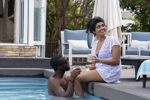 Multiethnic couple relaxing poolside with drinks on sunny backyard deck