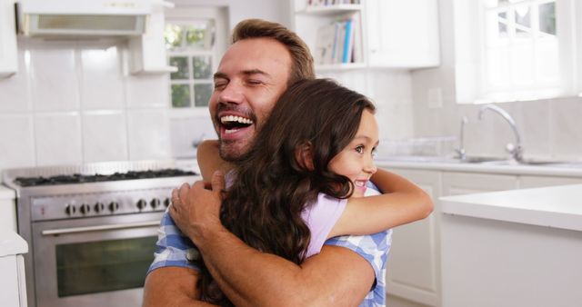 Father and daughter sharing a joyful hug in a bright, modern kitchen. Use this for family bonding concepts, parenting articles, advertisements promoting family values, or any content celebrating paternal relationships and the joy of family life.