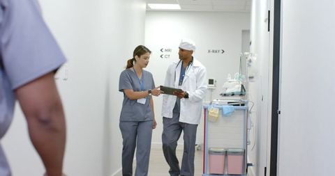 Hospital staff walking and reviewing tablet in corridor near mri ct x-ray signage