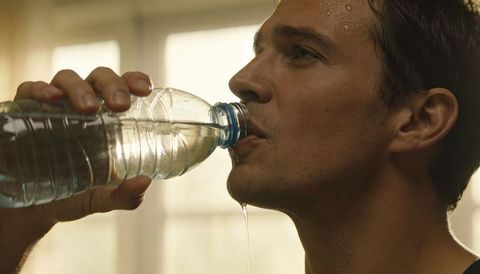 Shirtless man drinking water from plastic bottle at home after workout, sweaty closeup