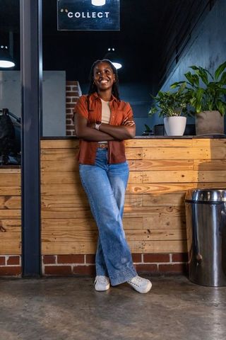 African american woman leaning on pickup counter smiling under collect sign in modern cafe