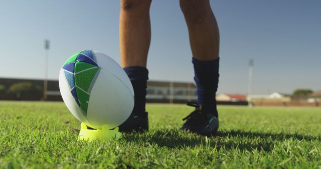 Rugby player prepares for a kick on the field, with copy space. Legs and rugby ball are in focus, emphasizing the sport's physicality.