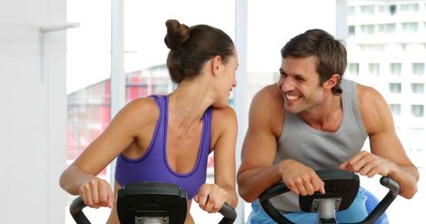 Couple Enjoying Exercise Bikes Together At Gym