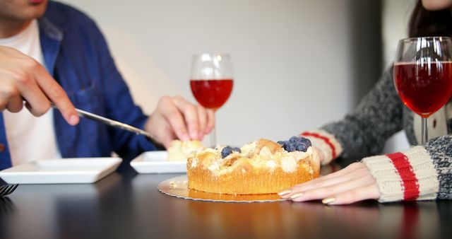 Couple sitting at a table enjoying a delicious cake and red wine. Ideal for use in lifestyle blogs, advertisements focusing on casual dining, celebrations or special moments together, and content promoting food and dining experiences.