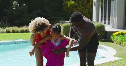 Family helping daughter dry off after swimming in home pool