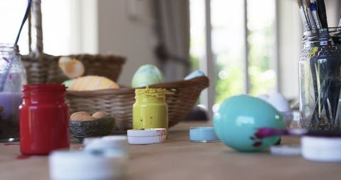 Hand Painting Pastel Easter Egg on Sunlit Craft Table with Bright Acrylic Paints