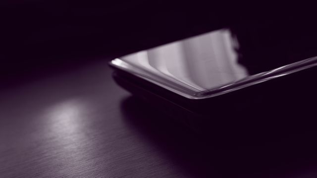 Close-up view of a glossy smartphone with light reflecting on its surface, placed on a dark surface. Ideal for use in articles and advertisements about modern technology, mobile devices, or digital communication trends.