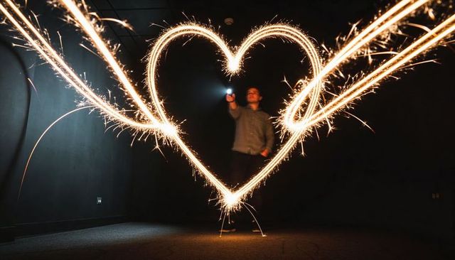 Man drawing glowing heart with sparkler long exposure light painting romantic sparks