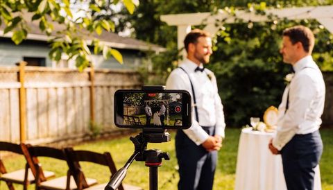 Smartphone recording backyard wedding ceremony between two grooms under pergola
