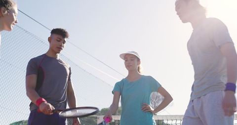 Diverse young tennis players gathering at net on sunny court sharing friendly doubles