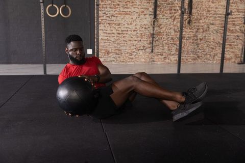 African american man performing russian twists holding medicine ball in brick gym interior