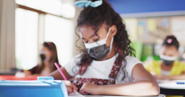 Young girl wearing a protective mask studying in a classroom. Image focuses on education during the pandemic. Suitable for articles on education, safety measures in schools, the impact of COVID-19 on learning, and children's health.