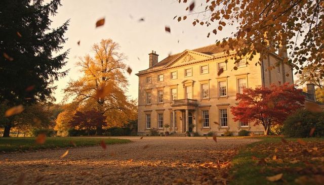 Neoclassical manor bathing in golden autumn light with falling leaves on gravel drive