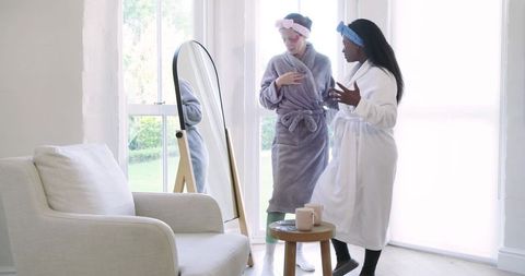 Diverse female friends adjusting wardrobe in sunlit living room