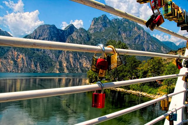 Love padlocks hanging on bridge railing with scenic mountainous lake view. Ideal for romantic, travel, and nature-related themes. Can be used for travel brochures, romantic getaway advertisements, and websites promoting scenic destinations.
