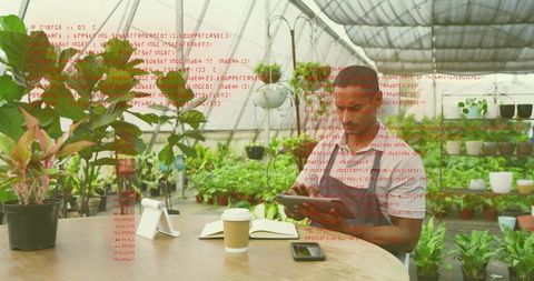 Greenhouse worker reviewing tablet notes at table with plants, coffee cup and smartphone