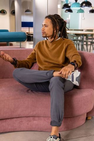 Young man with dreadlocks discussing ideas in modern coworking lounge on pink sofa