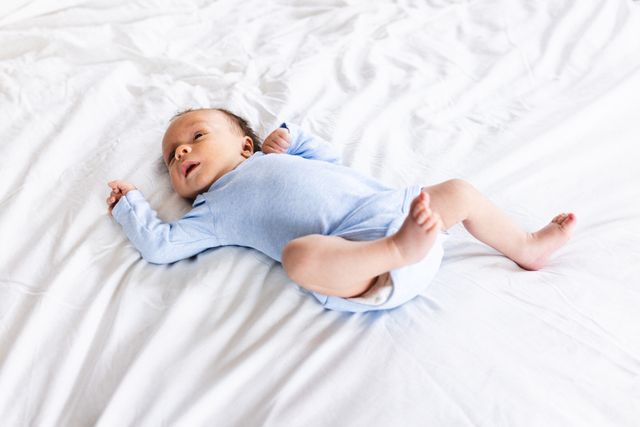 High angle view of cute newborn caucasian baby wearing blue clothes lying on bed at home. Copy space, unaltered, innocence, babyhood, new life, development.
