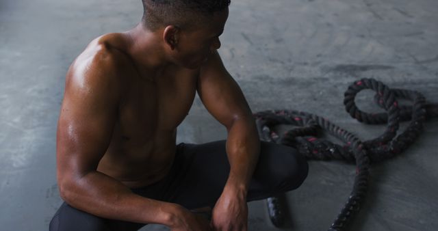 Shirtless african american man resting after battling ropes in an empty urban building. urban fitness and healthy lifestyle.