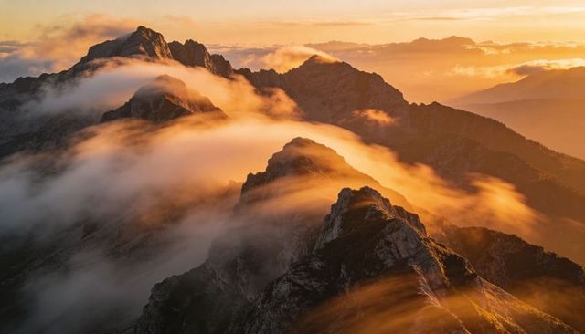 Golden hour fog cascading over alpine ridge, jagged peaks basking in warm light