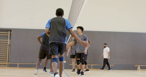 Diverse male volleyball team shaking hands at net in indoor gym court showing teamwork