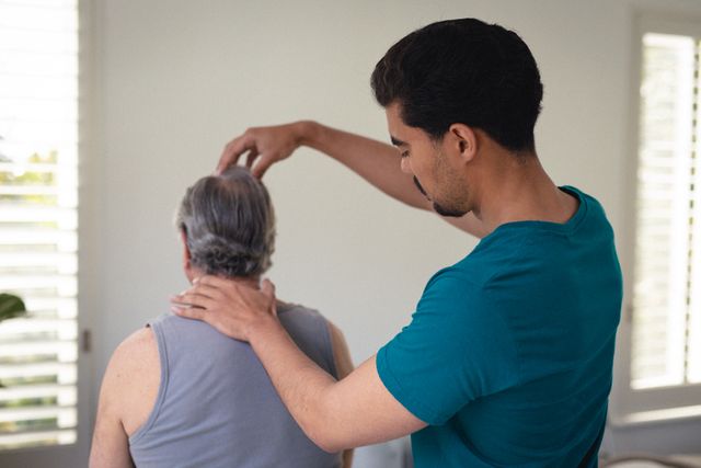 This image depicts a male physiotherapist providing a neck massage to a senior man at home, highlighting the concept of senior homecare and physical therapy. It can be used in articles or advertisements related to elderly care, home healthcare services, physical therapy, and wellness programs for seniors. The image emphasizes professional care and the importance of rehabilitation and pain relief for the elderly.