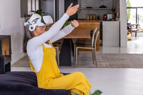 Senior woman experiencing virtual reality at home wearing vr headset and smartwatch